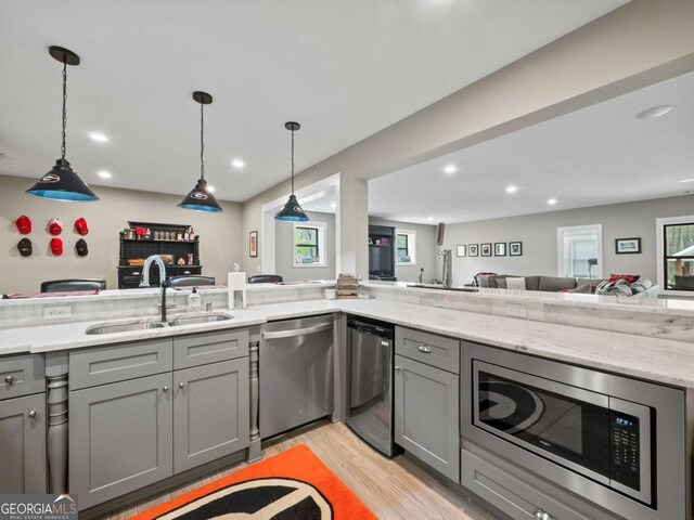 kitchen with stainless steel appliances, a sink, light stone counters, open floor plan, and gray cabinets