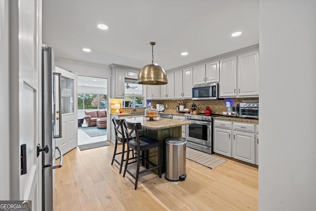 kitchen with appliances with stainless steel finishes, a sink, tasteful backsplash, light wood-style flooring, and a kitchen breakfast bar