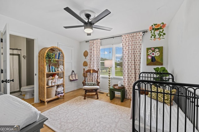 bedroom featuring a nursery area, light wood-style flooring, and ceiling fan