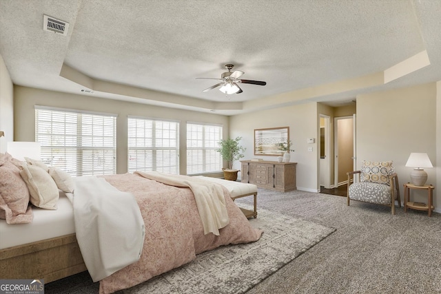 carpeted bedroom with a tray ceiling, a textured ceiling, baseboards, and visible vents