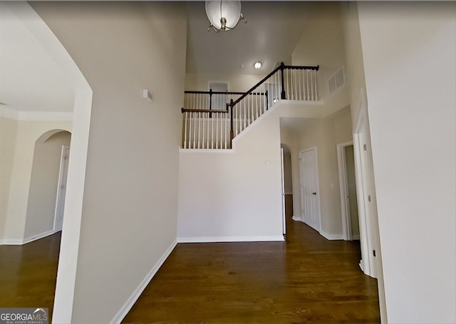 interior space featuring wood finished floors, visible vents, arched walkways, a high ceiling, and baseboards