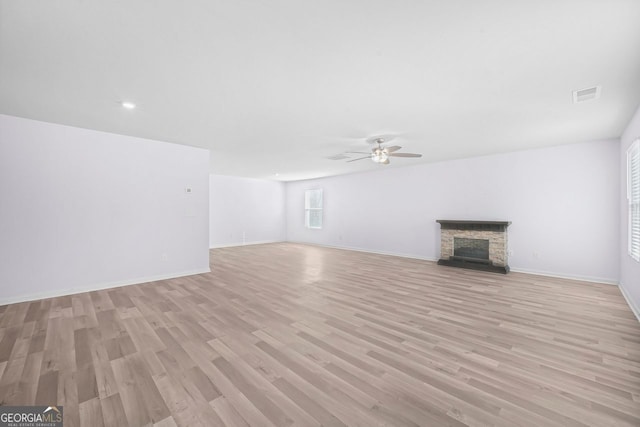 unfurnished living room featuring a fireplace, light wood-style flooring, a ceiling fan, visible vents, and baseboards