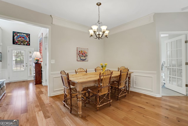 dining room featuring ornamental molding, wainscoting, a decorative wall, light wood-style flooring, and a notable chandelier
