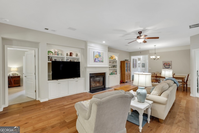 living area featuring visible vents, built in features, ceiling fan with notable chandelier, and light wood-style floors