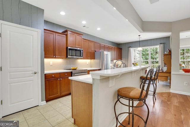 kitchen featuring brown cabinets, appliances with stainless steel finishes, a breakfast bar, light countertops, and a center island with sink