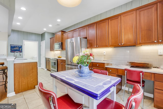 kitchen with light countertops, brown cabinets, a sink, backsplash, and stainless steel appliances