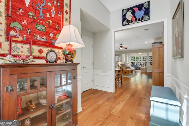 corridor featuring light wood-style floors, a decorative wall, and wainscoting