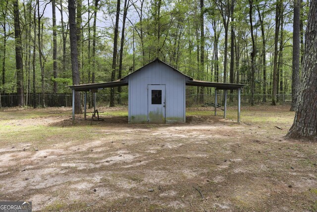 view of shed with a wooded view, a detached carport, and fence