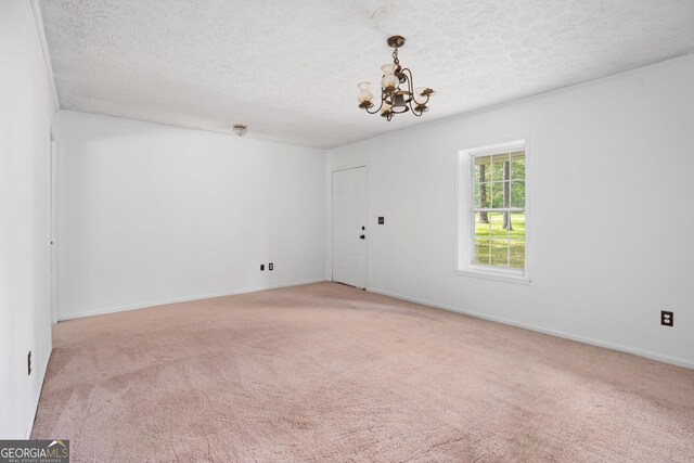 carpeted empty room with a chandelier, baseboards, and a textured ceiling