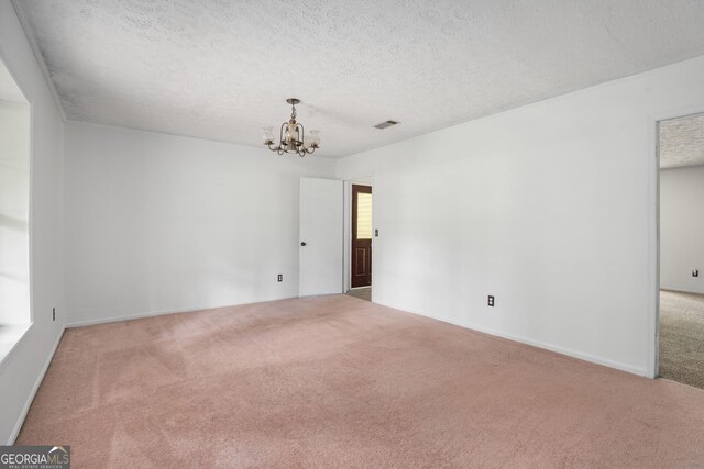 spare room with visible vents, an inviting chandelier, a textured ceiling, and carpet