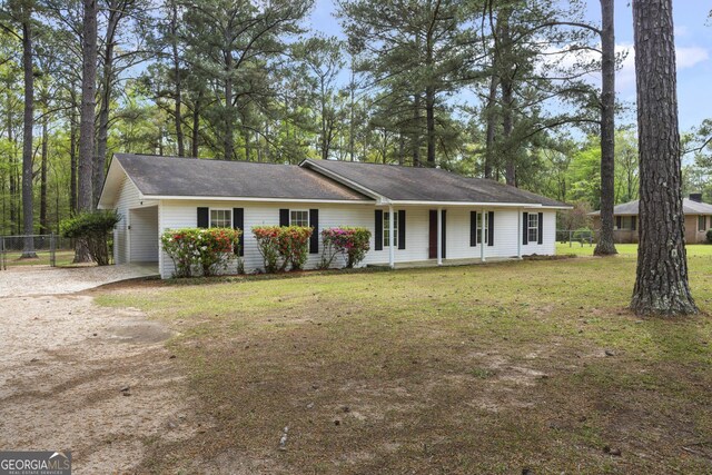 ranch-style home featuring dirt driveway, an attached carport, covered porch, fence, and a front lawn
