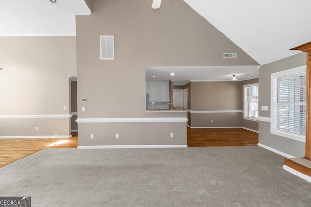 unfurnished living room with carpet flooring, high vaulted ceiling, baseboards, and visible vents