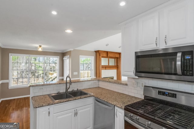 kitchen featuring decorative backsplash, appliances with stainless steel finishes, a sink, white cabinetry, and a peninsula