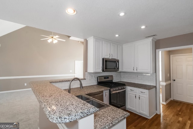 kitchen featuring decorative backsplash, white cabinets, a sink, appliances with stainless steel finishes, and a peninsula