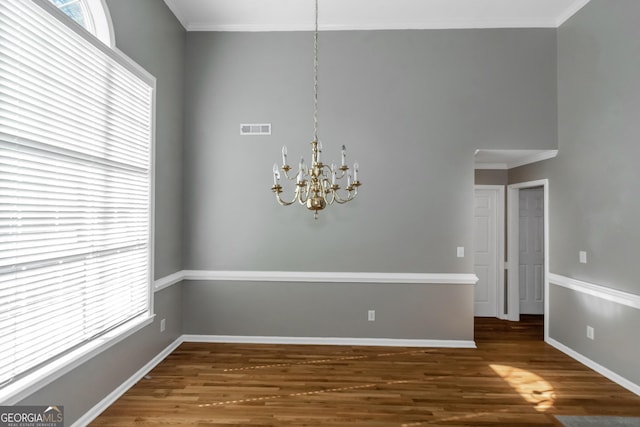 unfurnished dining area featuring wood finished floors, baseboards, visible vents, a notable chandelier, and crown molding