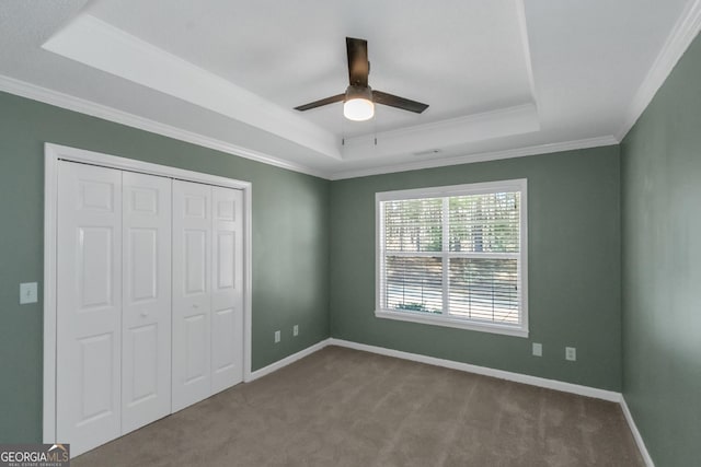 unfurnished bedroom featuring crown molding, a tray ceiling, baseboards, and carpet floors