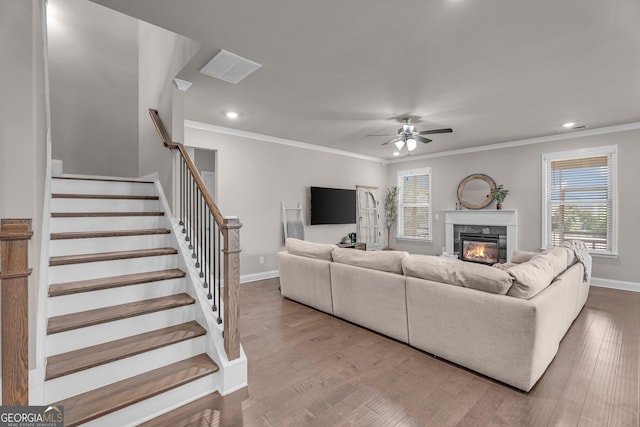 living room featuring a glass covered fireplace, plenty of natural light, crown molding, and a ceiling fan