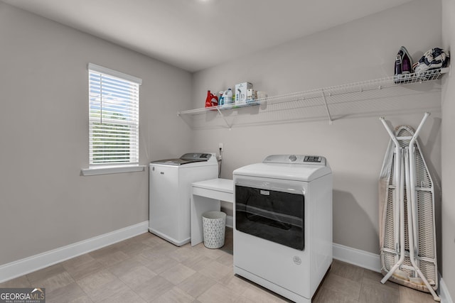 clothes washing area with light floors, separate washer and dryer, baseboards, and laundry area