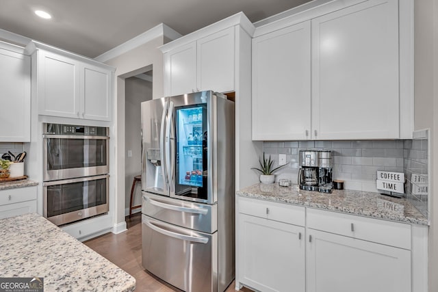 kitchen featuring white cabinets, stainless steel appliances, wood finished floors, and backsplash