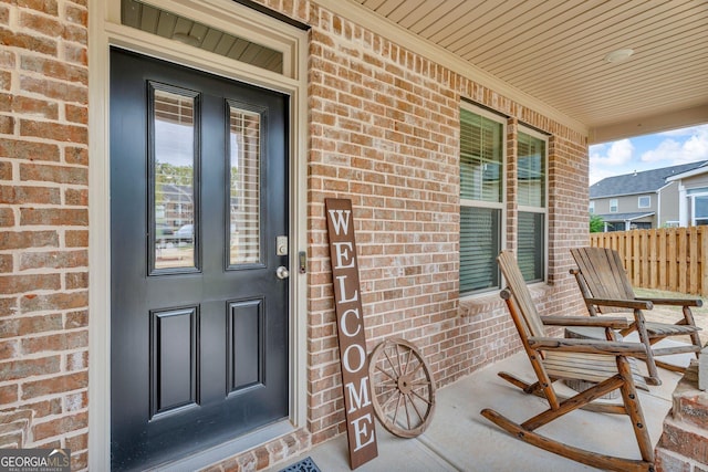 view of exterior entry with a porch, fence, and brick siding