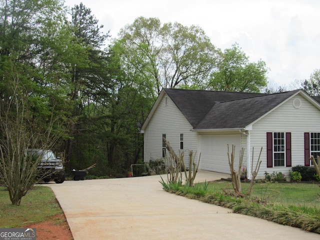 view of home's exterior featuring concrete driveway, roof with shingles, a garage, and a lawn