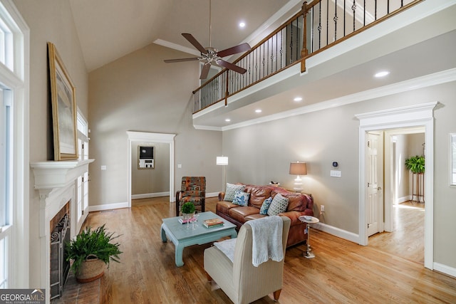 living area with baseboards, light wood-type flooring, ceiling fan, and high vaulted ceiling