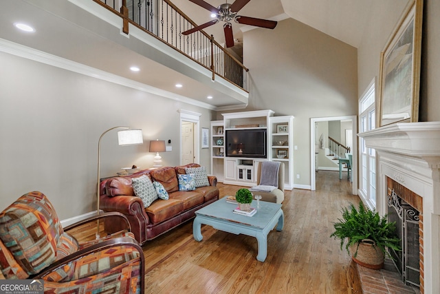 living room featuring a high ceiling, a fireplace, a ceiling fan, baseboards, and wood finished floors