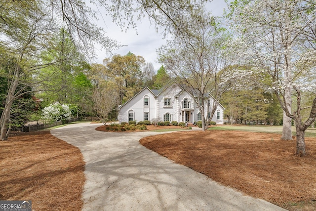 view of front of property with stucco siding, curved driveway, and fence