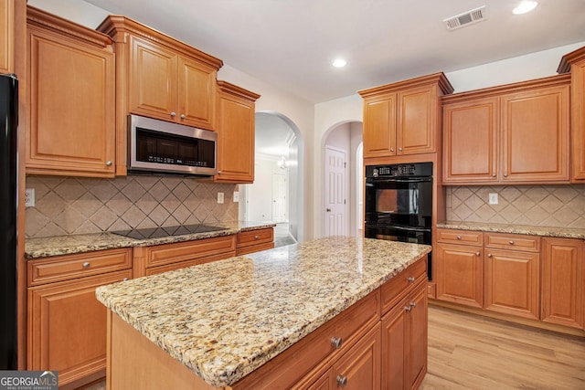 2036 Broadmoor Way, Fairburn, GA 30213 - kitchen with light wood finished floors, light stone countertops, visible vents, black appliances, and arched walkways