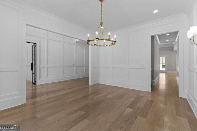 unfurnished dining area featuring a decorative wall, ornamental molding, wood finished floors, recessed lighting, and a notable chandelier