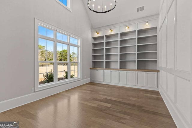 empty room featuring an inviting chandelier, baseboards, built in shelves, visible vents, and wood finished floors