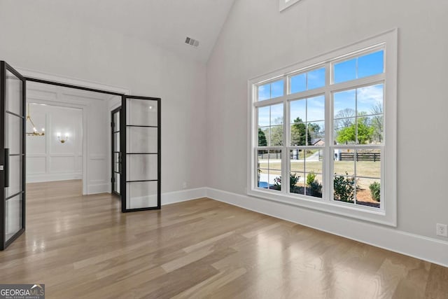 empty room with baseboards, visible vents, a notable chandelier, and light wood finished floors