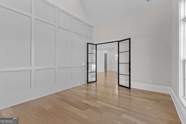 unfurnished bedroom featuring a decorative wall, baseboards, vaulted ceiling, and light wood-type flooring