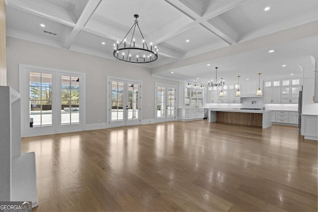 unfurnished living room featuring coffered ceiling, a notable chandelier, beam ceiling, french doors, and wood finished floors