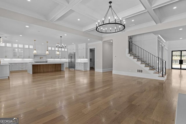 unfurnished living room featuring a notable chandelier, coffered ceiling, stairway, and visible vents