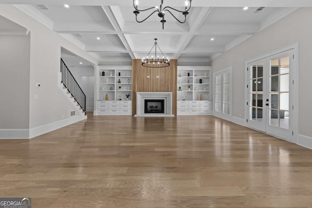 unfurnished living room with coffered ceiling, a notable chandelier, wood finished floors, and built in shelves
