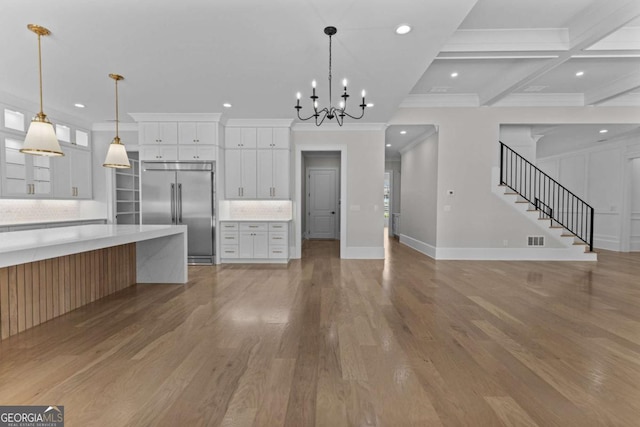 kitchen featuring light countertops, light wood finished floors, built in refrigerator, glass insert cabinets, and an inviting chandelier