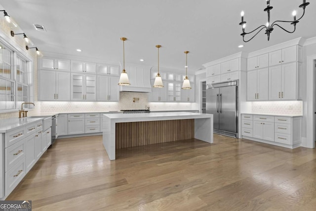 kitchen with light countertops, stainless steel built in fridge, light wood-type flooring, and custom range hood