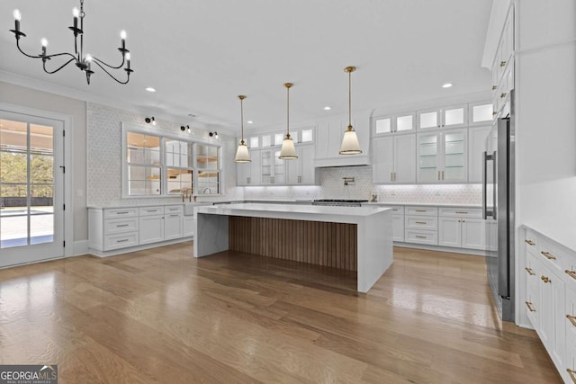 kitchen with stainless steel refrigerator, light countertops, a chandelier, white cabinets, and decorative backsplash