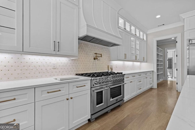 kitchen with visible vents, custom exhaust hood, crown molding, white cabinetry, and double oven range