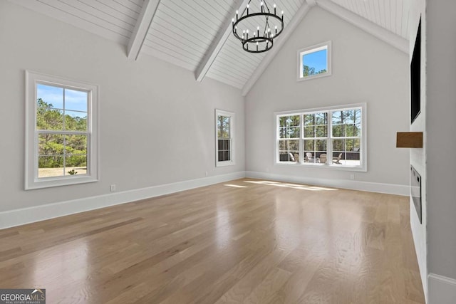 unfurnished living room featuring baseboards, beamed ceiling, wood finished floors, and a notable chandelier