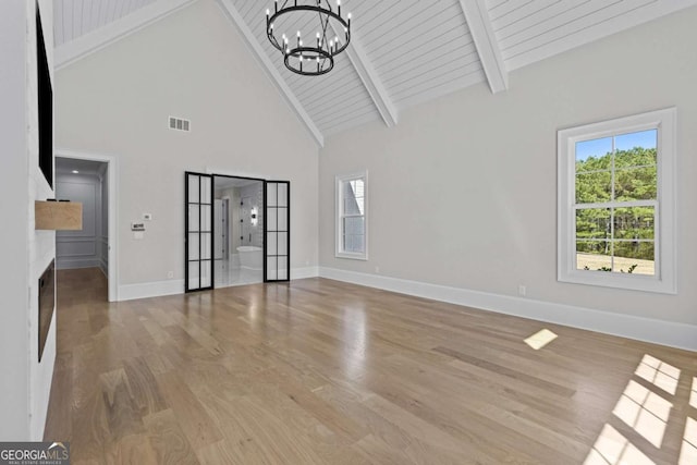 unfurnished living room with beam ceiling, baseboards, a chandelier, and light wood-type flooring