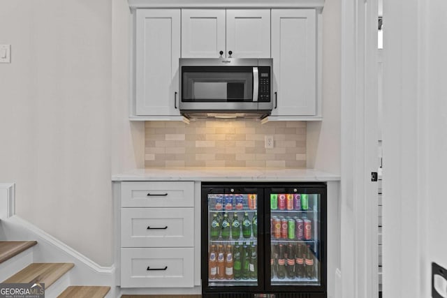 bar with stairs, backsplash, beverage cooler, stainless steel microwave, and baseboards