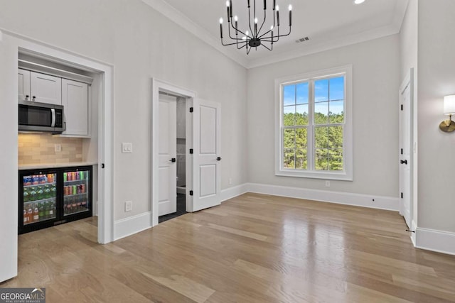unfurnished dining area featuring baseboards, a notable chandelier, crown molding, and light wood-type flooring
