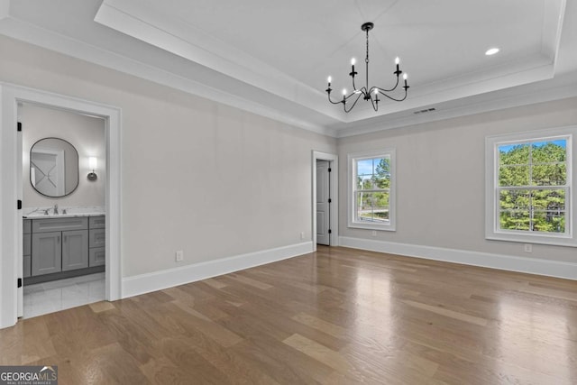 unfurnished dining area featuring a tray ceiling, a sink, and an inviting chandelier