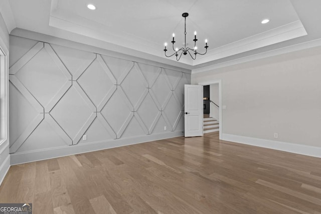unfurnished dining area featuring an inviting chandelier, a raised ceiling, baseboards, and light wood-type flooring