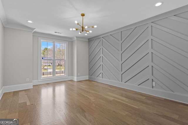 empty room with ornamental molding, visible vents, a decorative wall, a notable chandelier, and wood finished floors