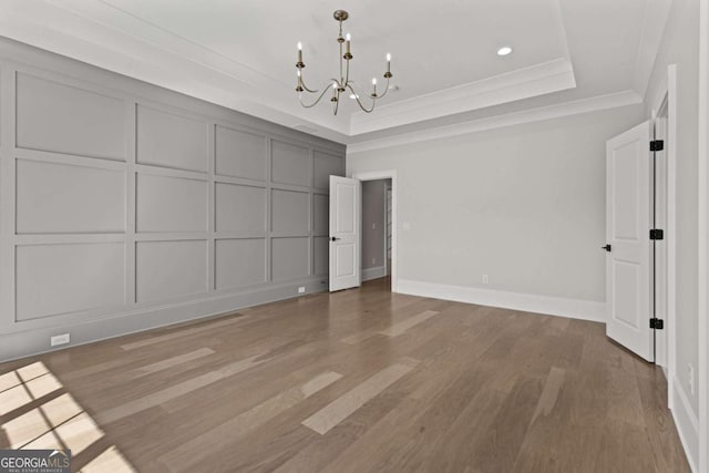 interior space with crown molding, a raised ceiling, a decorative wall, a notable chandelier, and wood finished floors