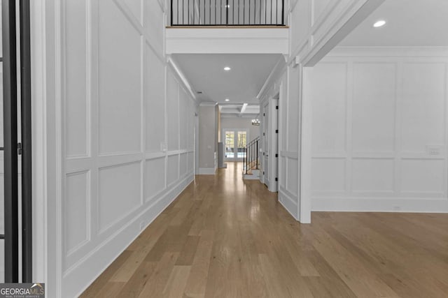 corridor featuring stairway, a decorative wall, recessed lighting, and light wood-style floors