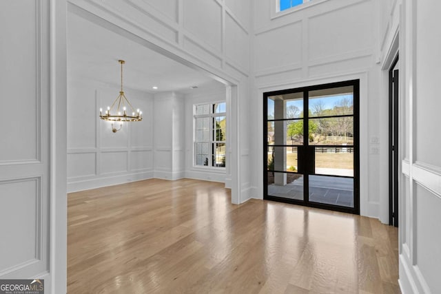 unfurnished dining area featuring a decorative wall, a healthy amount of sunlight, a chandelier, and light wood finished floors